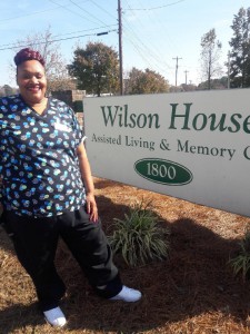 Ezrosta Faison stands in front of the sign for her employer Wilson House Assisted Living & Memory Center. Faison is a recent graduate of the Wilson Housing Authority's Family Self-Sufficiency program who has moved into her residence after going through five eye surgeries to allow her to regain her sight.