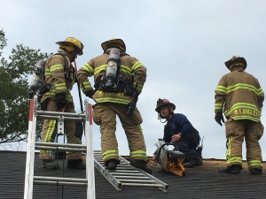 Firefighter demo photo 3: Wilson Fire/Rescue Services Engineer Roger Godwin, Firefighter Micah Varnell and Captain Mike Langley listen as Captain Jim Miller, crouching in blue shirt, gives instructions about how to properly saw a hole in the top of a building when it is needed. They were involved in training at Wilson Housing Authority buildings that are abandoned and slated for demolition.